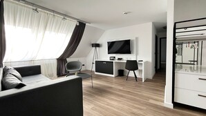 A modern living room with a sofa, a desk, and a TV. -  DORMERO Hotel Xanten (Xanten)