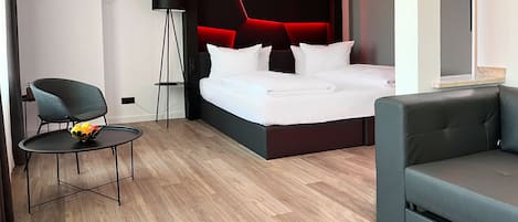 A modern hotel room with a bed, a chair, a small table, and a floor lamp.