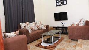 Una sala de estar con un sofá marrón, una mesa de centro de vidrio, un televisor de pantalla plana y una alfombra estampada.