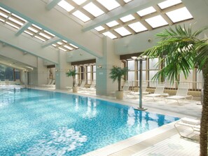 Una piscina interior con agua cristalina, rodeada de sillones de descanso y plantas en macetas.