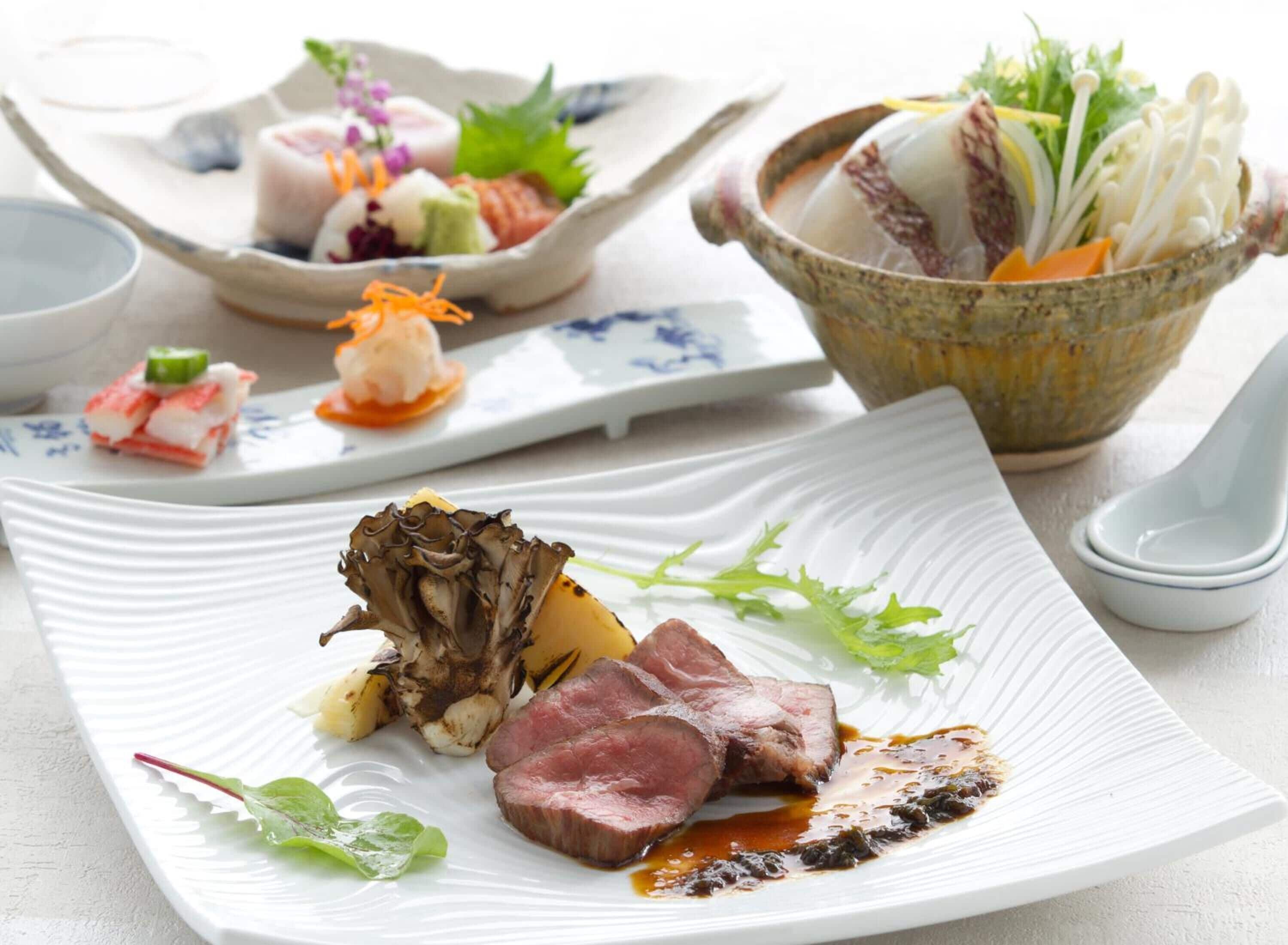 A variety of dishes on a table, including a plate with sliced meat, roasted potatoes, and greens, and another plate with sushi and vegetables.
