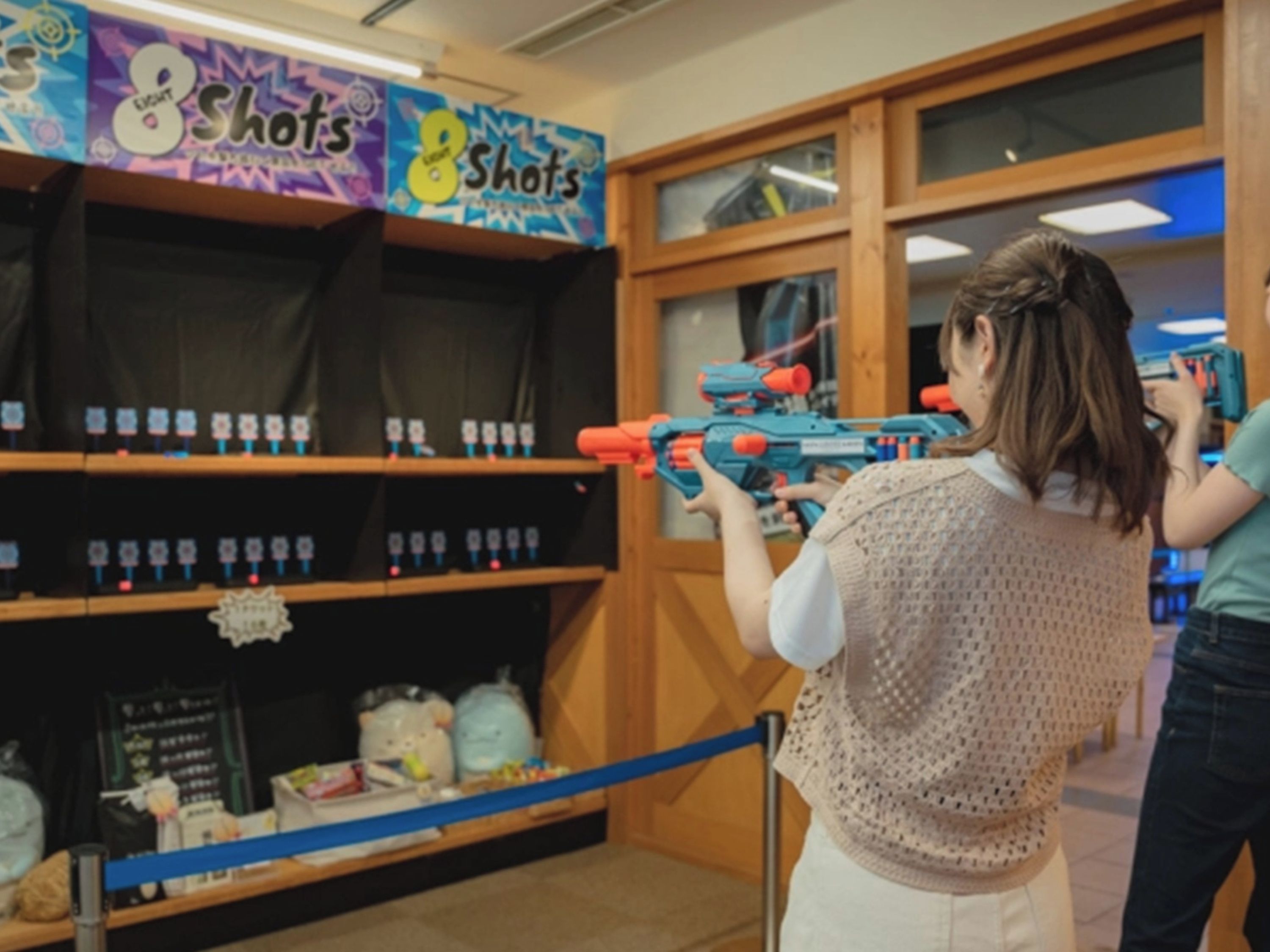 A person holding a toy gun in a room with shelves containing various items.