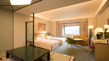Een hotelkamer met twee bedden, een bureau, een stoel, een klein tafeltje en een raam met gordijnen.