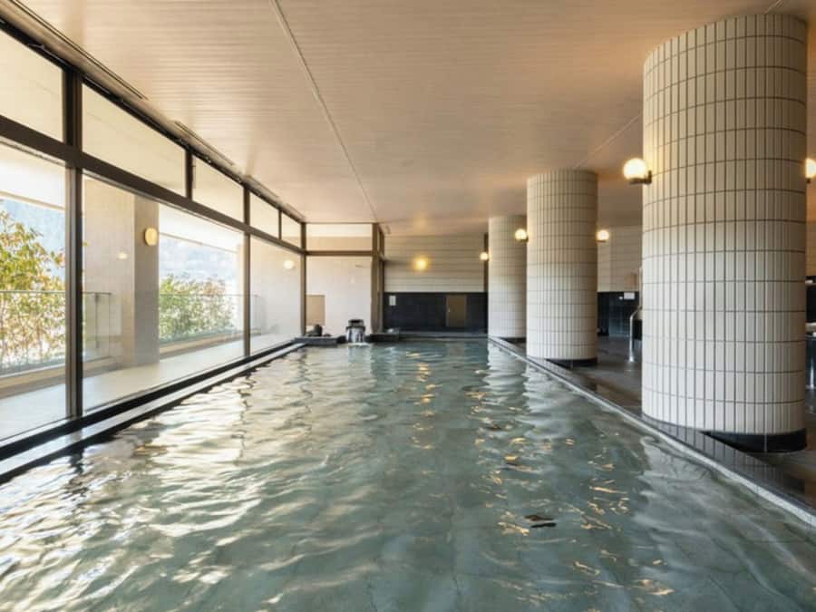 En indendørs swimmingpool med glasvægge, flisegulv og et loft med indbygningsspots.