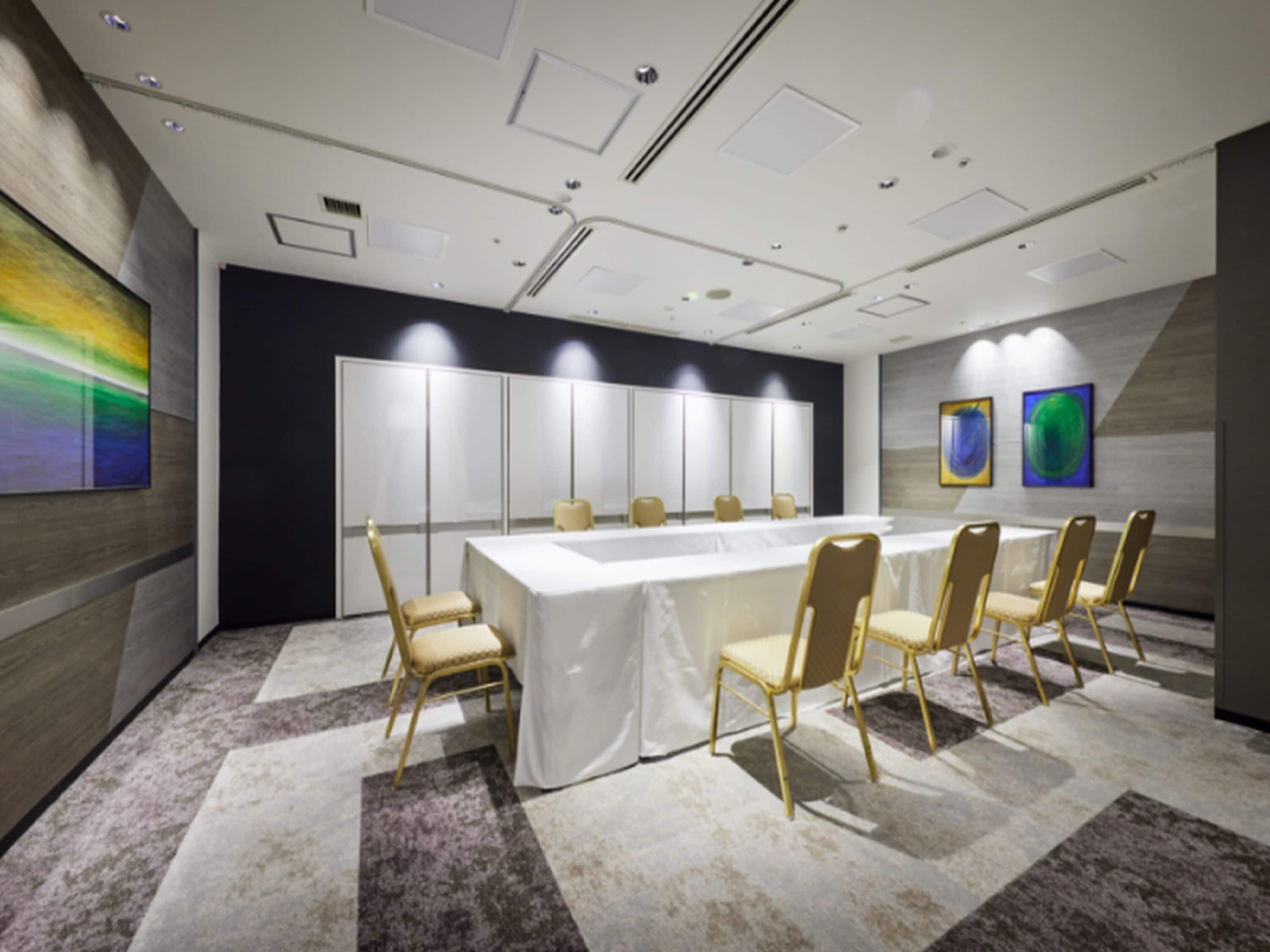 A conference room with a long table, chairs, a white tablecloth, and artwork on the walls.