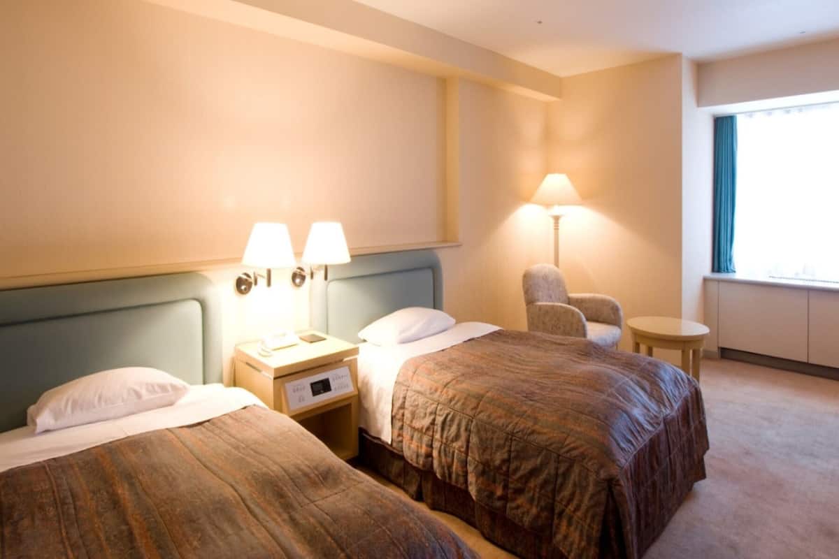 Une chambre d’hôtel avec deux lits, une chaise, une lampe et une fenêtre.