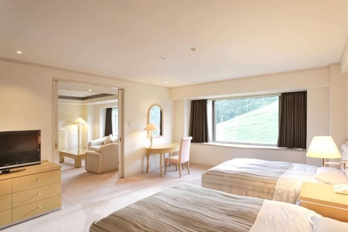 A hotel room with a bed, a desk, a chair, a TV, and a window.