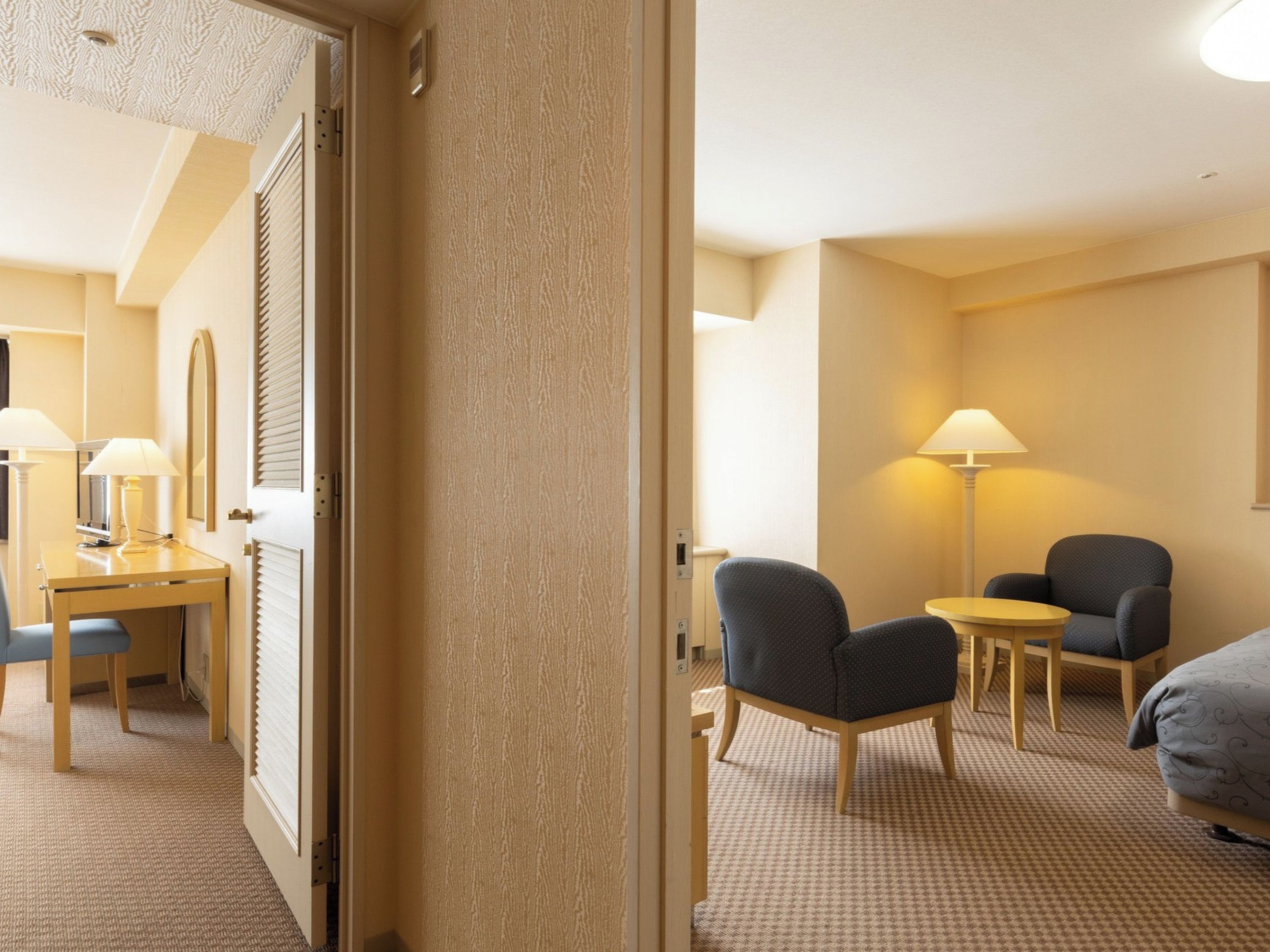 Habitación de hotel con escritorio, dos sillas, cama y lámpara.