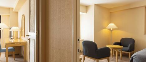 Habitación de hotel con escritorio, dos sillas, cama y lámpara.