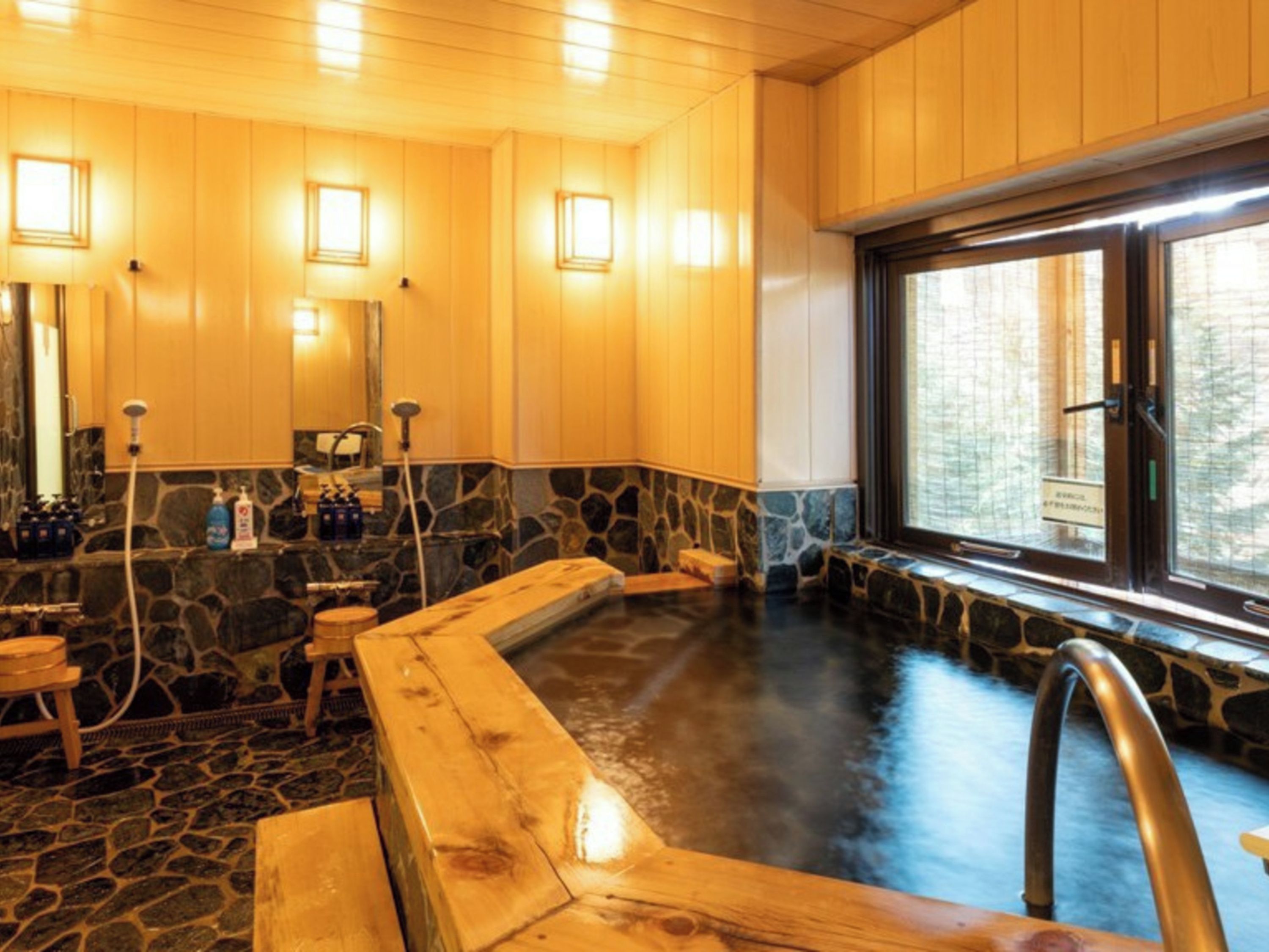 A wooden interior with a stone-tiled hot tub, wooden benches, and a window with a view.