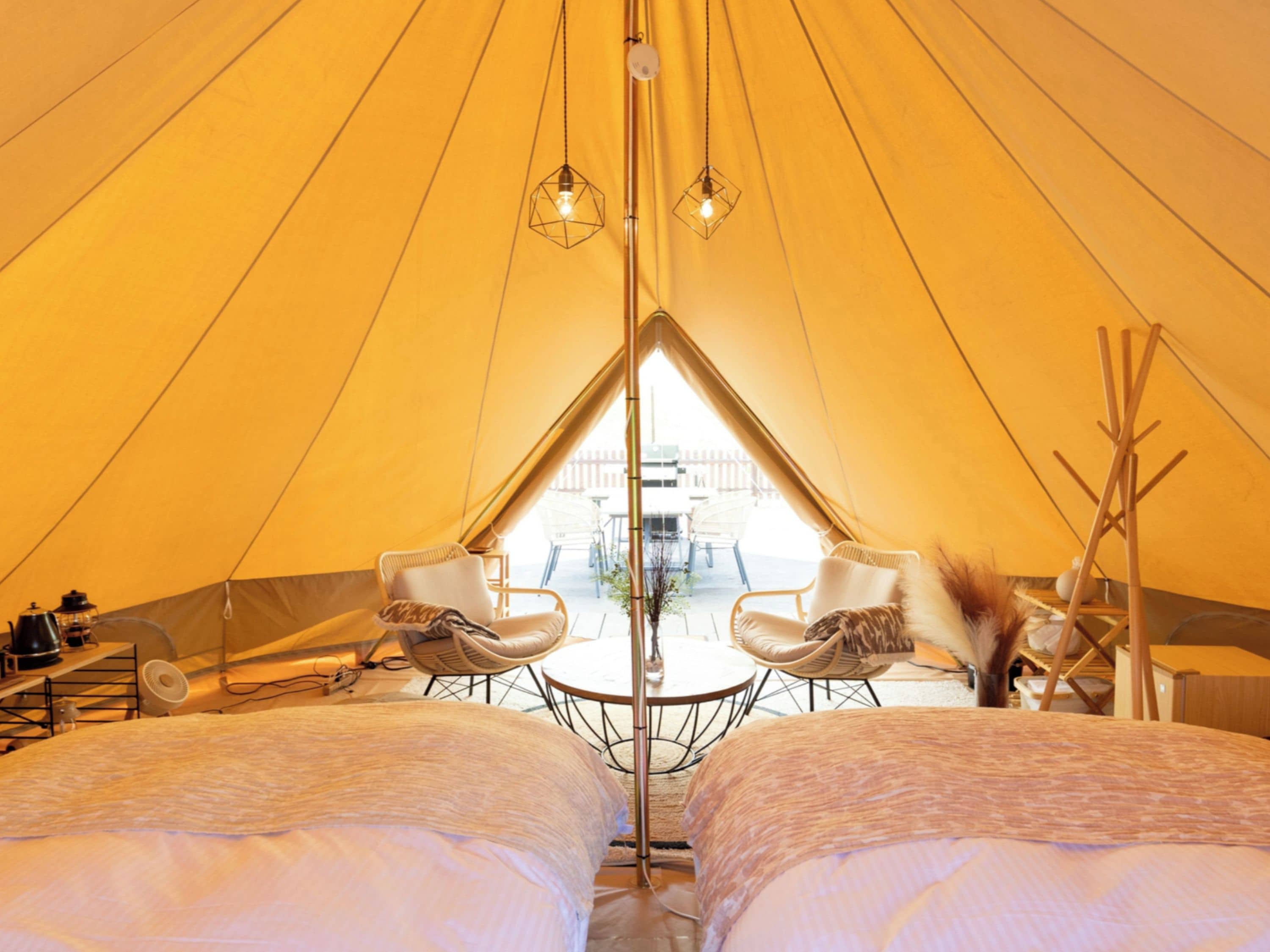Una carpa con dos camas, una mesa, sillas y luces colgantes.
