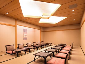 Una habitación con suelo de esteras de tatami, mesas y sillas de madera dispuestas en filas.