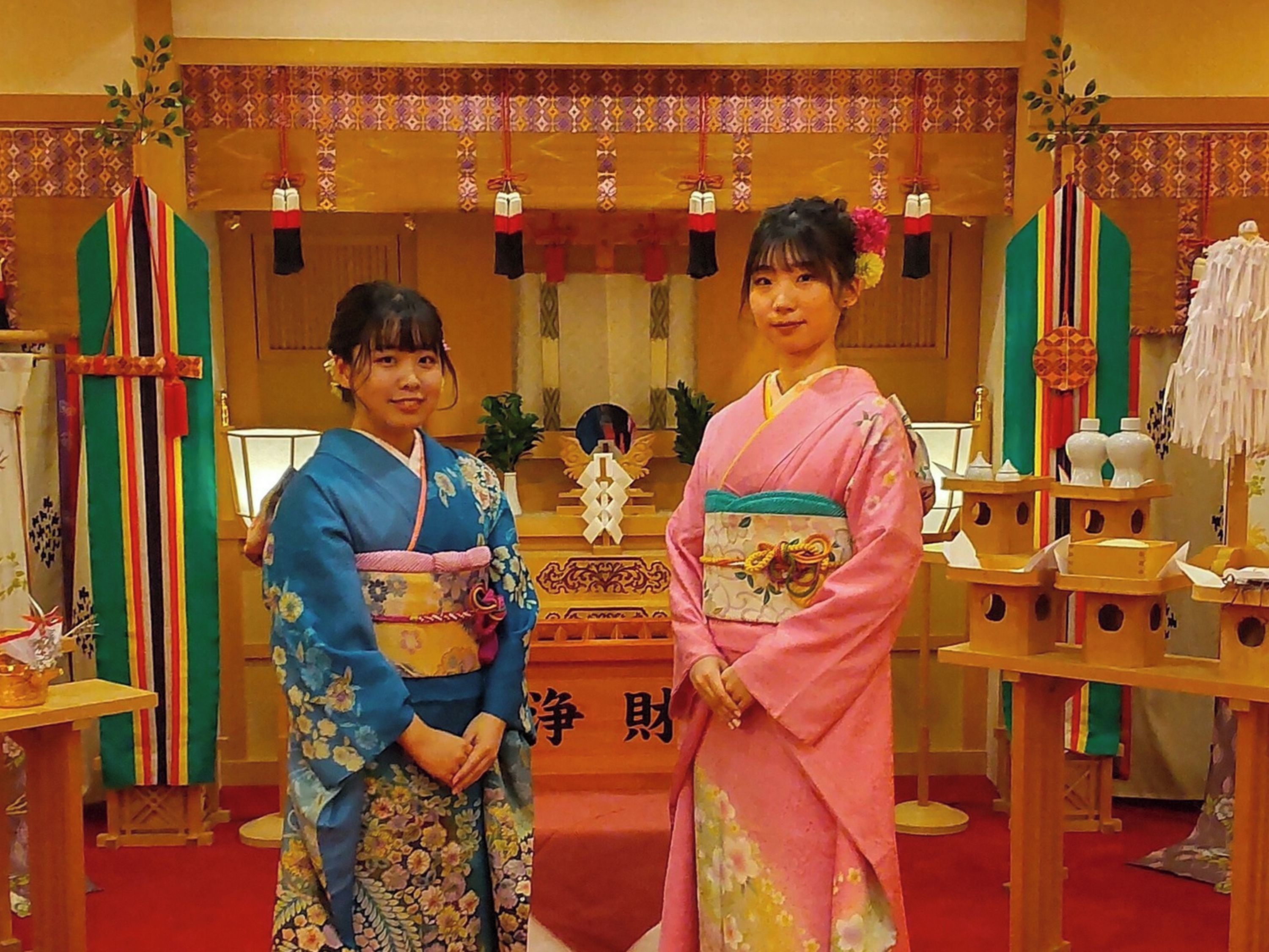 Two individuals in traditional attire standing in a room with a wooden altar and various ceremonial items.