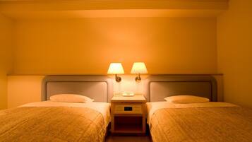 Una habitación de hotel con dos camas individuales, una mesita de noche con lámpara, y una lámpara de pared.