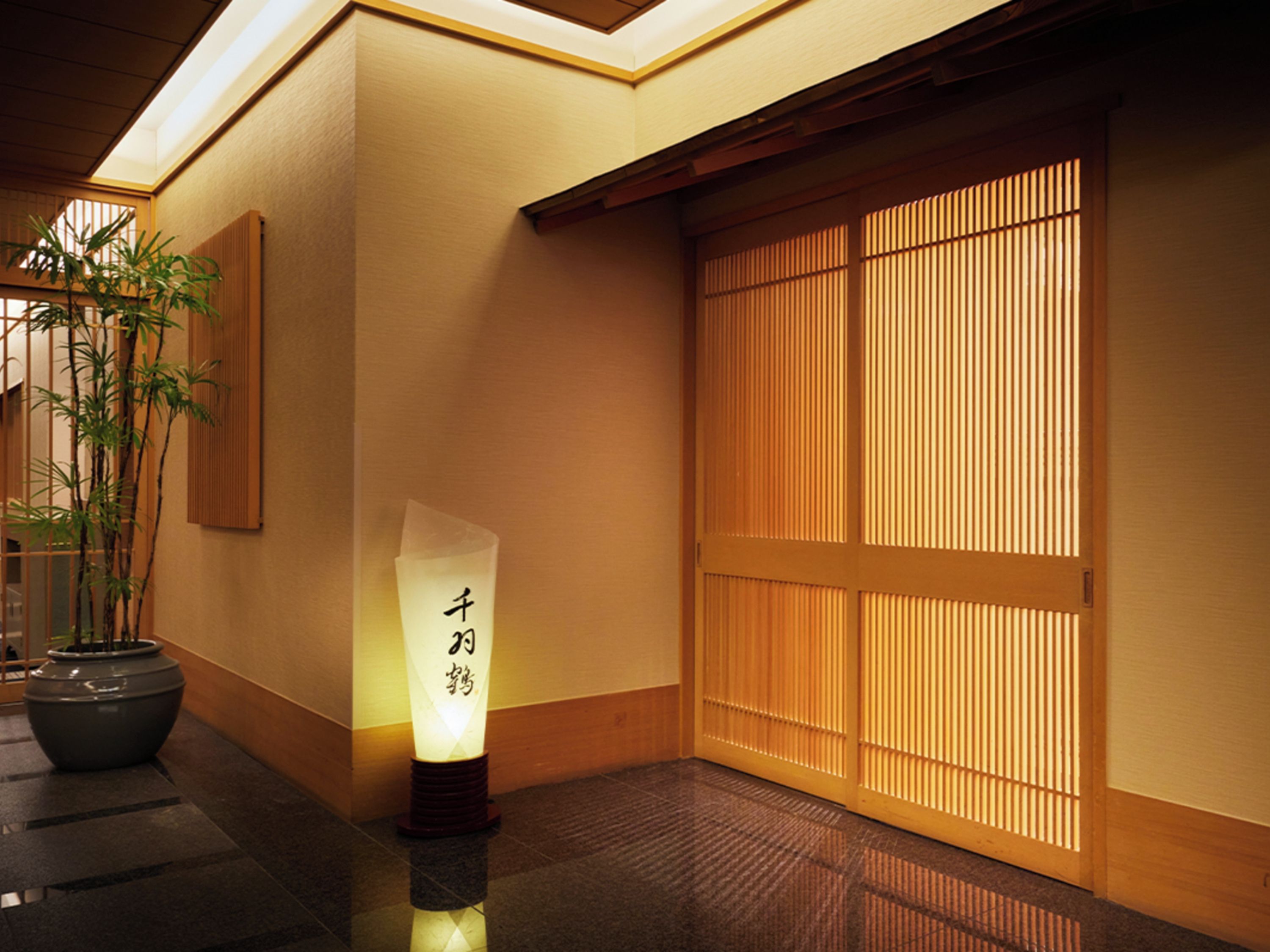 A traditional Japanese interior with tatami flooring, a shoji screen door, and a bamboo plant.