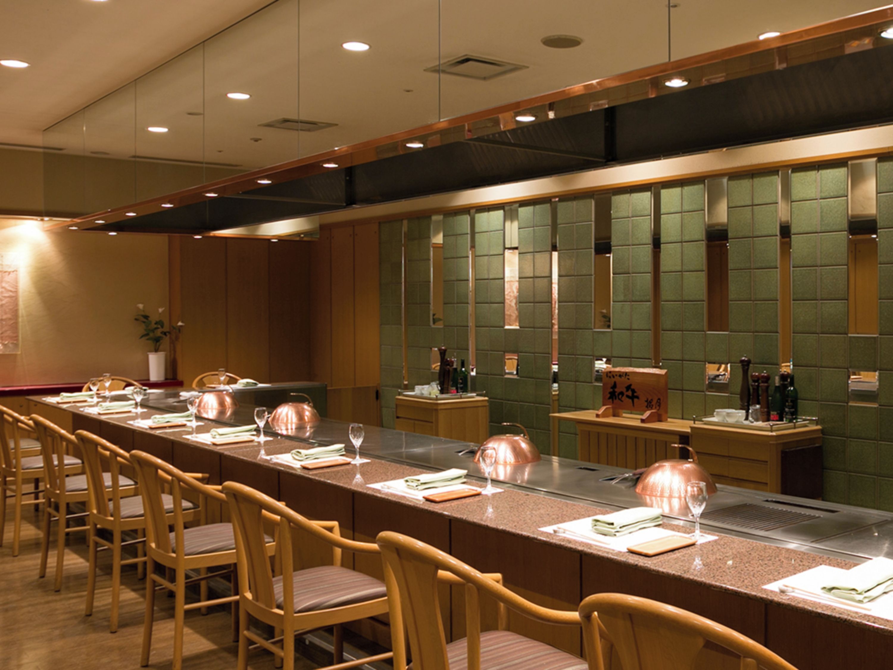 A long dining table with chairs, a bar area, and a green partition wall with a grid pattern.