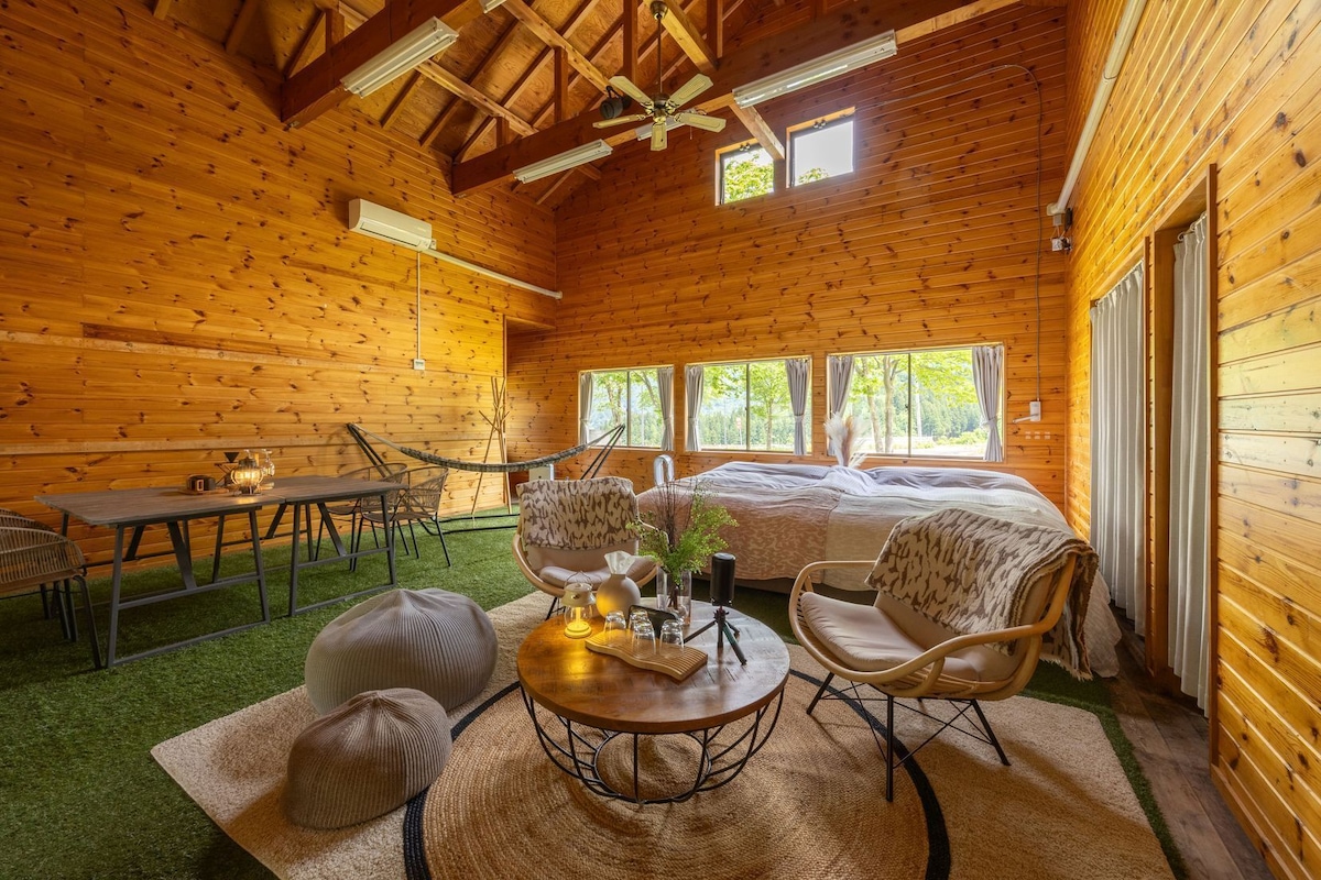 A log cabin interior with a dining area, a seating area with a table and chairs, and a large bed.