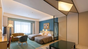 Een hotelkamer met twee bedden, een bureau, een stoel, een salontafel en een groot raam met gordijnen.
