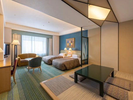A hotel room with two beds, a desk, a chair, a coffee table, and a large window with curtains.