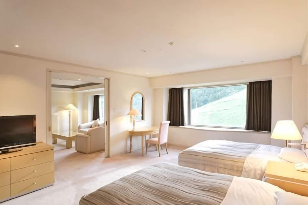 Une chambre d’hôtel avec deux lits, une télévision, un bureau avec une chaise, une lampe et une grande fenêtre.