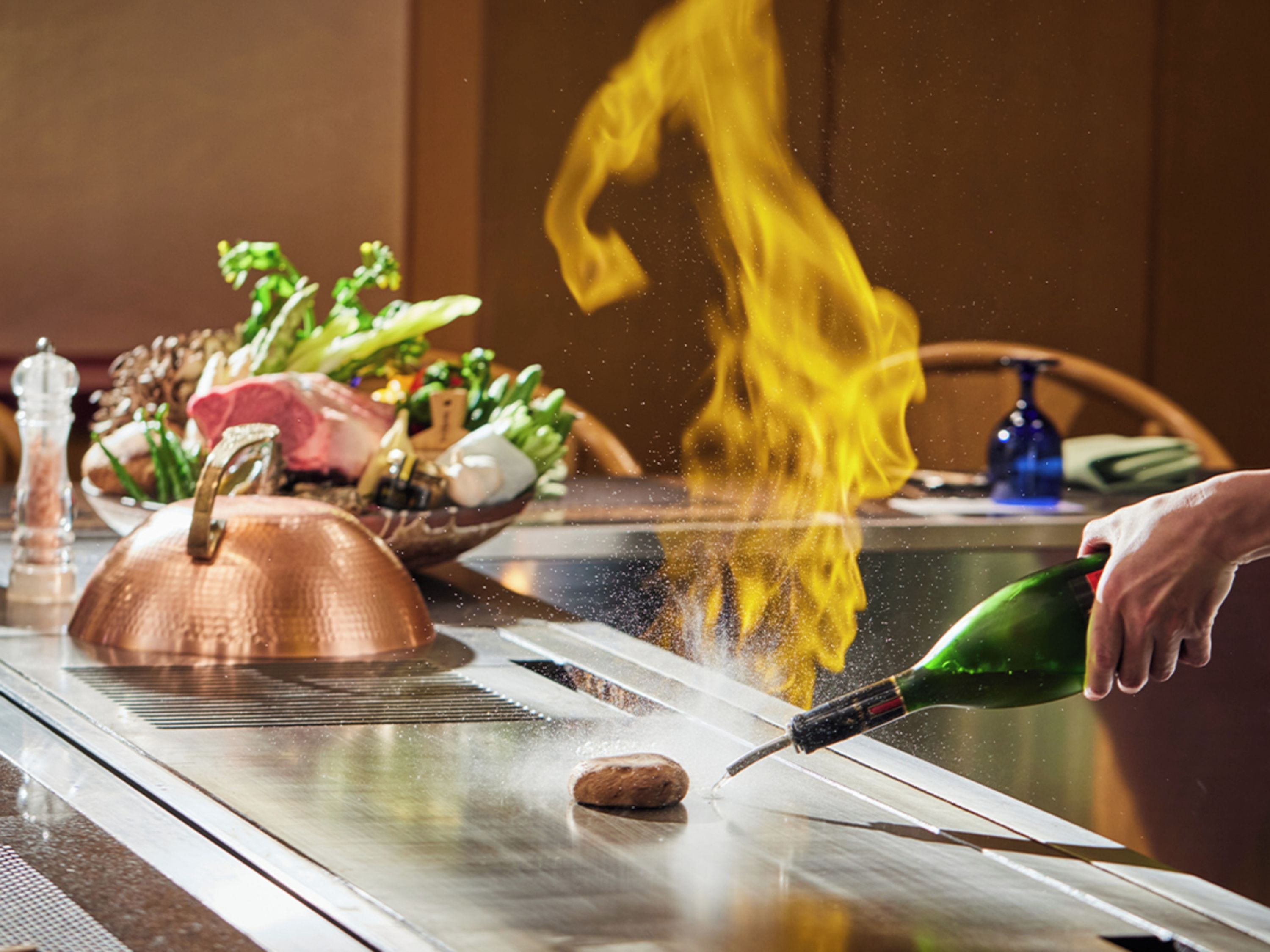 A table with a copper pot, a bottle of sauce, and a flame.