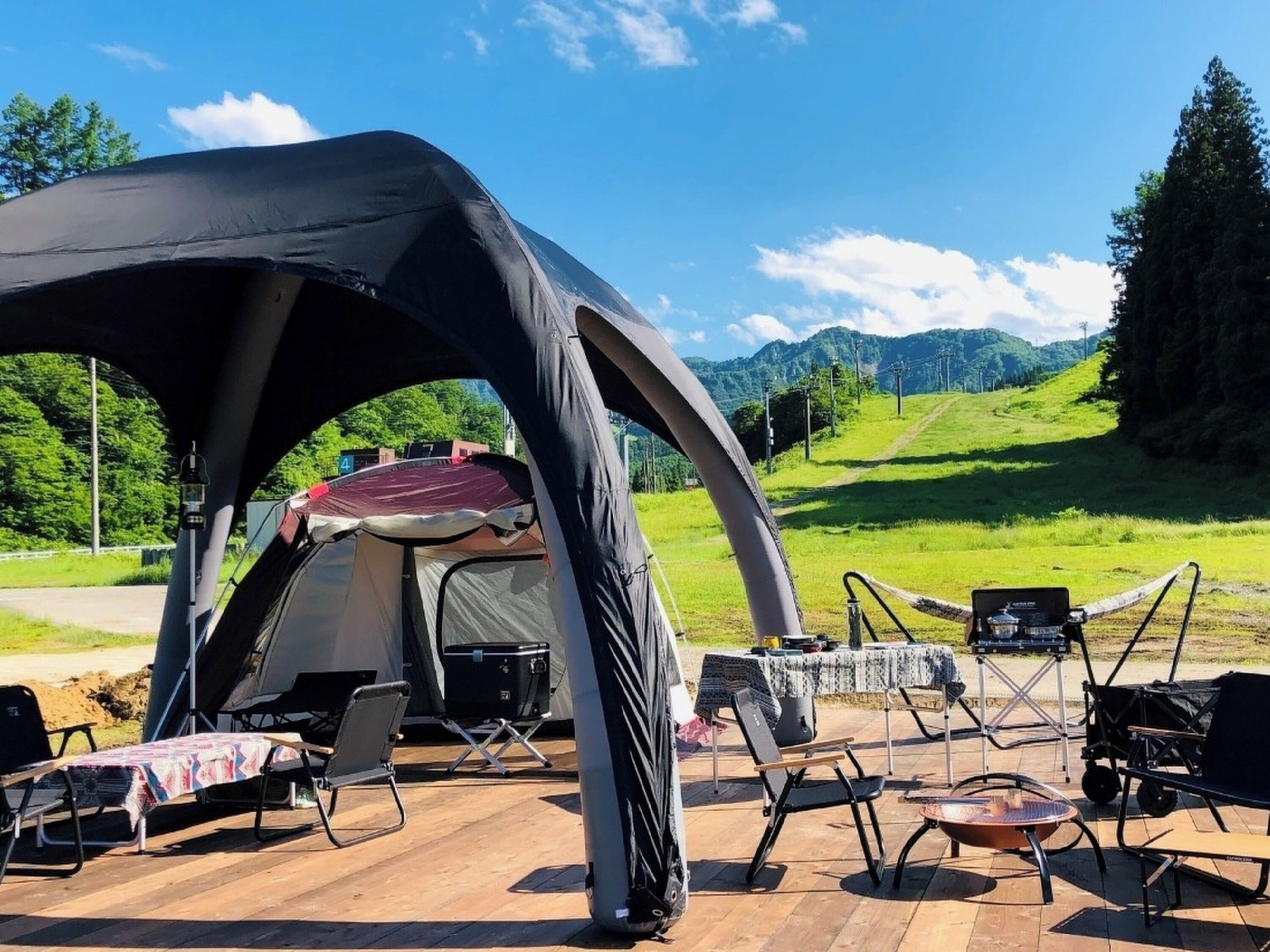 A camping setup with a tent, chairs, and a table on a wooden deck with a scenic mountain view.