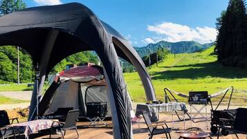 A camping setup with a tent, chairs, and a table on a wooden deck with a scenic mountain view.