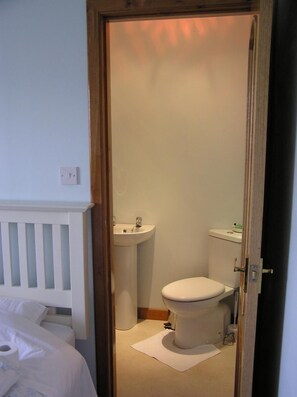 A small, clean bathroom with a toilet, sink, and a white toilet paper roll on the floor. - The Antlers (Lybster)