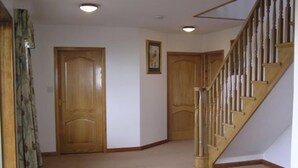 A hallway with wooden doors, a staircase with wooden railings, and a carpeted floor. - The Antlers (Lybster)