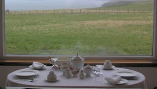 A table set with fine china and teapots, overlooking a grassy field and a distant view of a body of water. - The Antlers (Lybster)