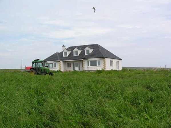 A house with a sloped roof and a green tractor in a grassy field. - The Antlers (Lybster)