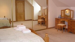 A bedroom with a large mirror, a wooden dresser, a bedside table, and a bed with neatly folded towels. - The Antlers (Lybster)
