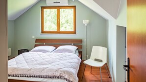 A bedroom with a wooden bed, a white chair, a window, and an air conditioning unit. - Roso 3 bedroom modern country house (gmina Chynów)