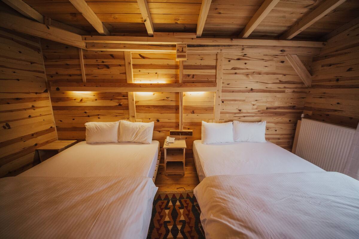 Quarto de cabana de madeira com duas camas, uma mesa de cabeceira e um aplique na parede.