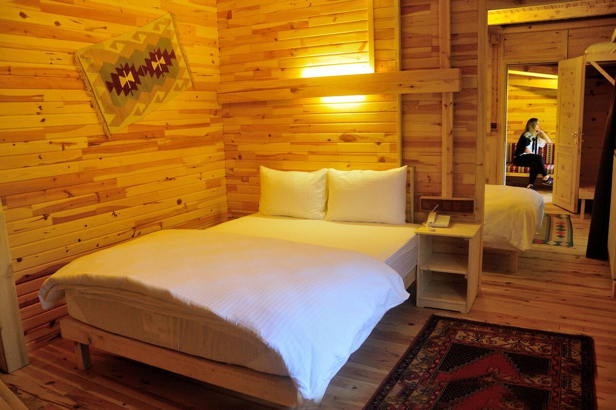 Quarto com painéis de madeira, uma cama, mesa de cabeceira e espelho.