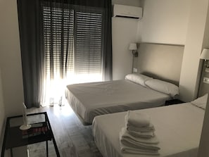 A hotel room with two beds, a bedside table with a lamp, a window with blinds, and an air conditioning unit. - Hotel Boutique Centro BBB (Benidorm)