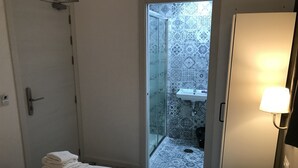 Une chambre d’hôtel avec un lit, une salle de bain aux carreaux décoratifs, un lavabo et une table de chevet avec une lampe.
