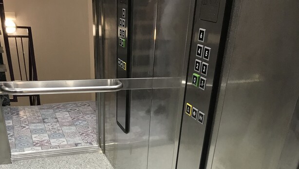 L’intérieur d’un ascenseur, avec un revêtement métallique, une barre de maintien et un panneau de commande doté de boutons permettant de sélectionner les étages.