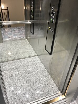 Een liftinterieur met een metalen afwerking, een handgreep en een bedieningspaneel met knoppen voor verdiepingsselectie.