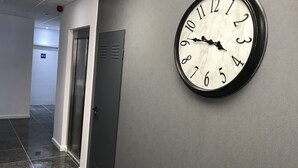 Un couloir avec une horloge au mur, une porte et une pancarte portant le numéro 002.