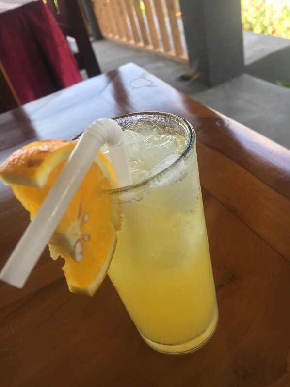 Un vaso de limonada con hielo y una pajita, decorado con una rodaja de naranja, sobre una mesa de madera.