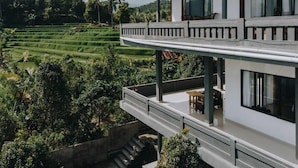 Un bâtiment à deux étages doté d’un balcon donnant sur des champs en terrasses et une montagne.