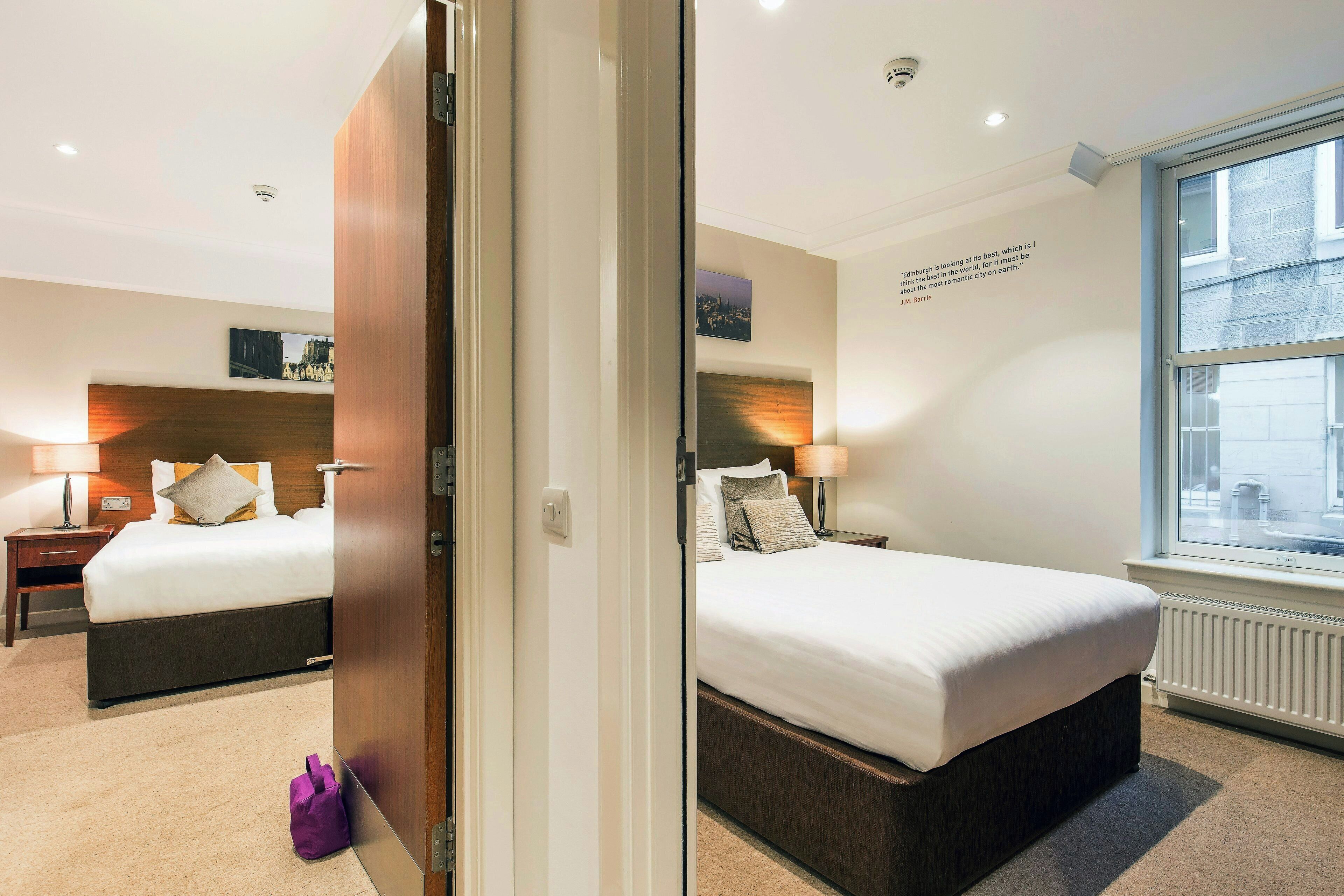 A hotel room with a bed, bedside tables, a window, and a door.