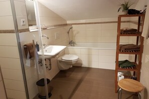 Un baño con cabina de ducha de vidrio, un lavamanos, un inodoro y un estante de madera con toallas.