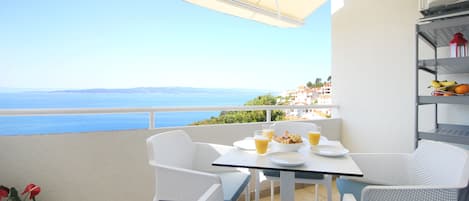 A balcony with a table set for breakfast, overlooking a coastal view.