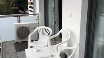En balkon med to hvide plastikstole og et lille bord, et vindue og en dør.