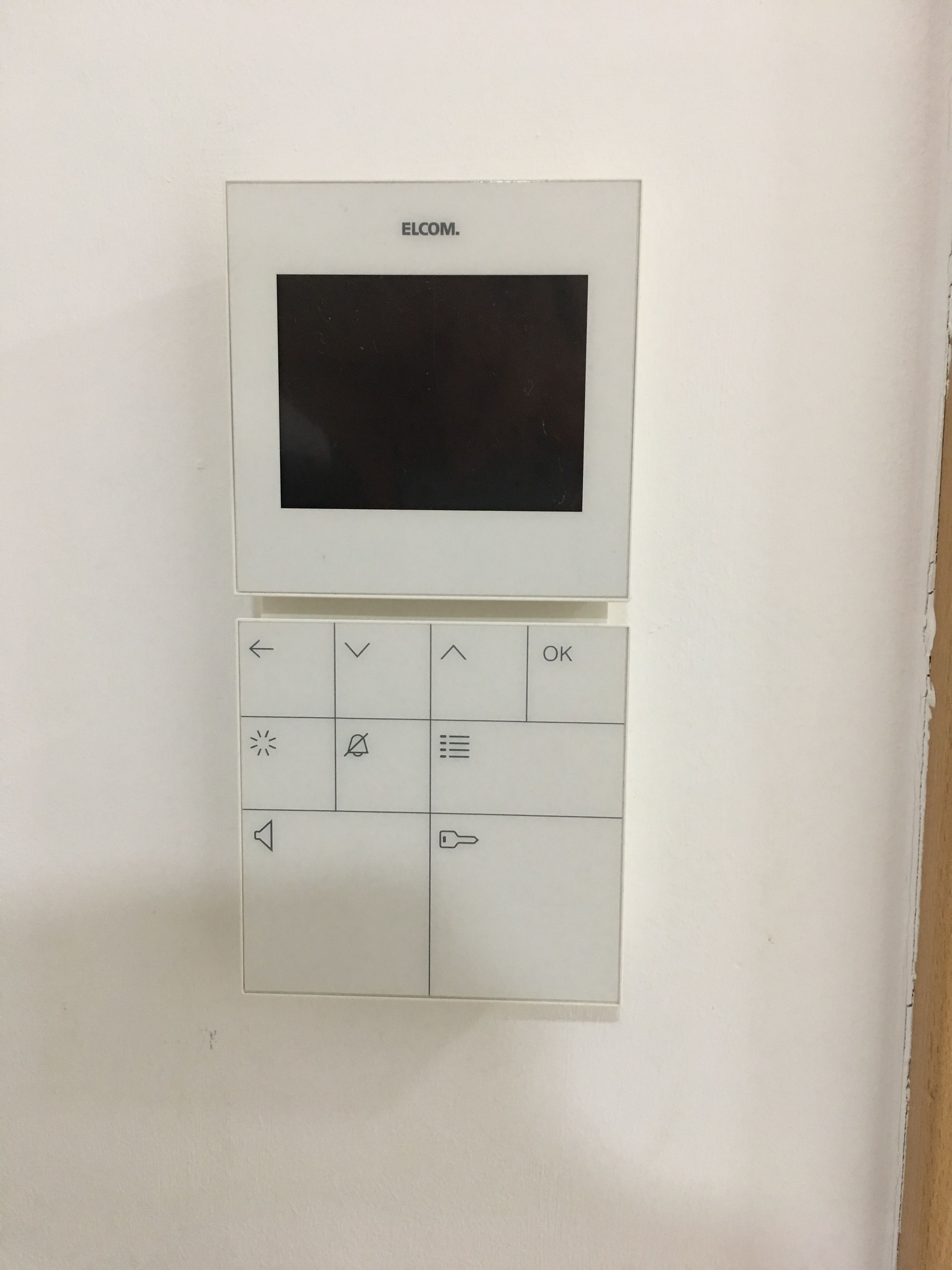 Un dispositivo ELCOM fijado a la pared con una pantalla y varios botones de control.