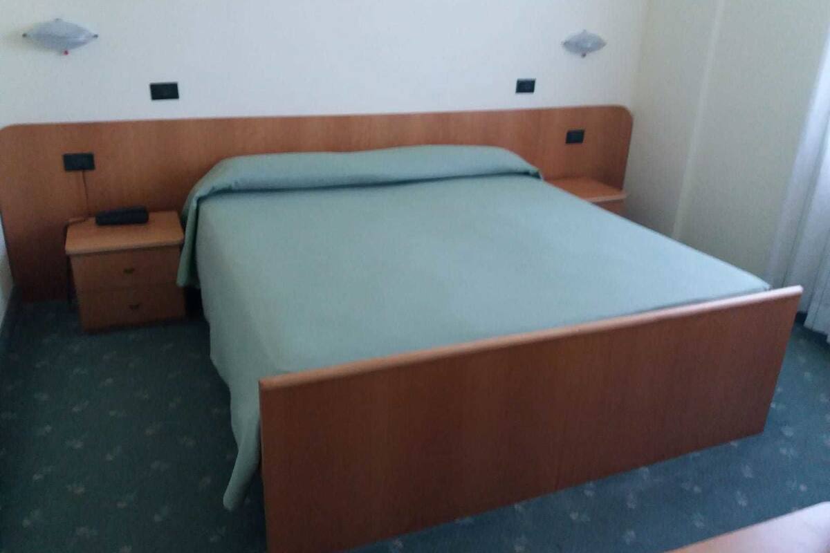A standard hotel room with a single bed, a nightstand, a drawer, and a small table.