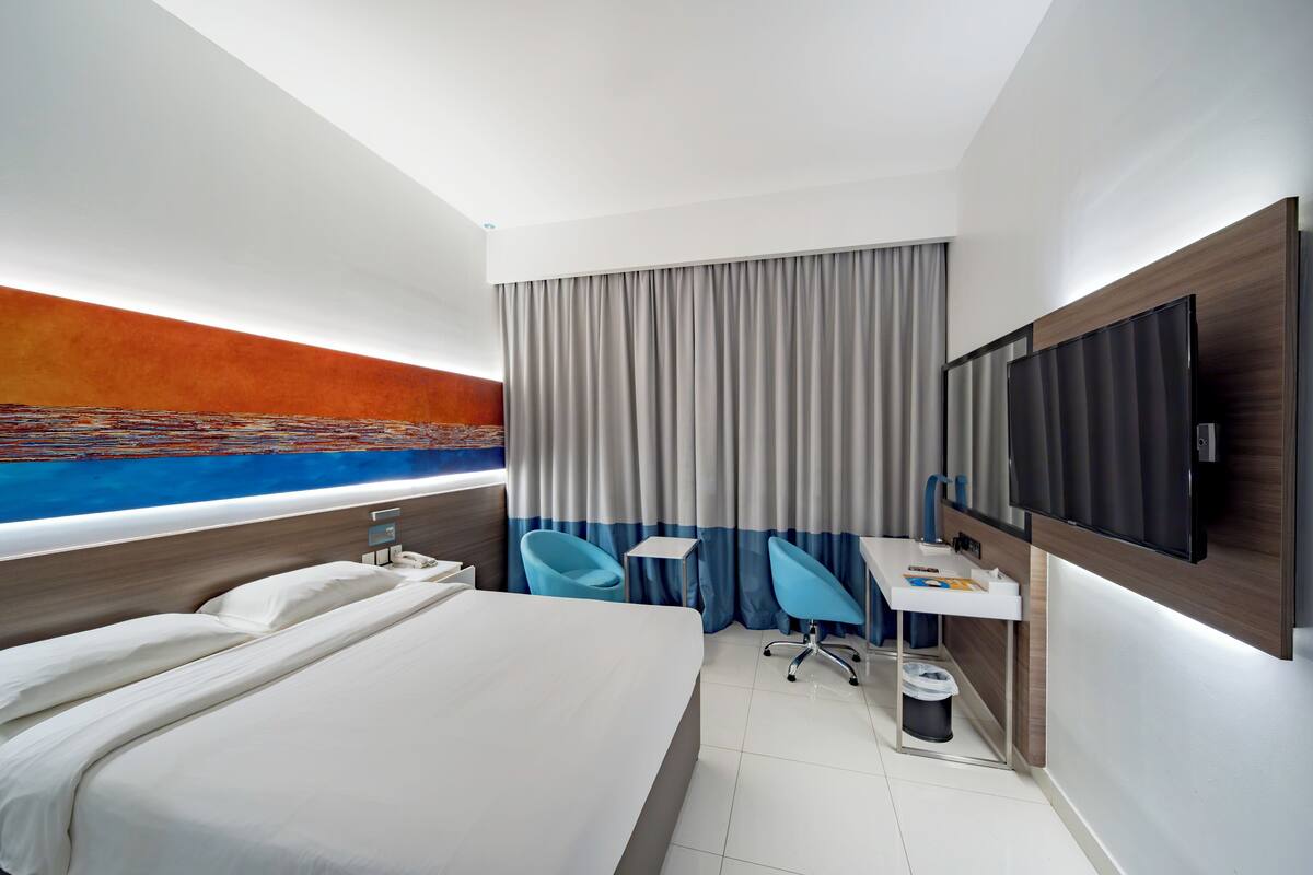 A modern hotel room with a large bed, a desk, a chair, a TV, and a view of the ocean.