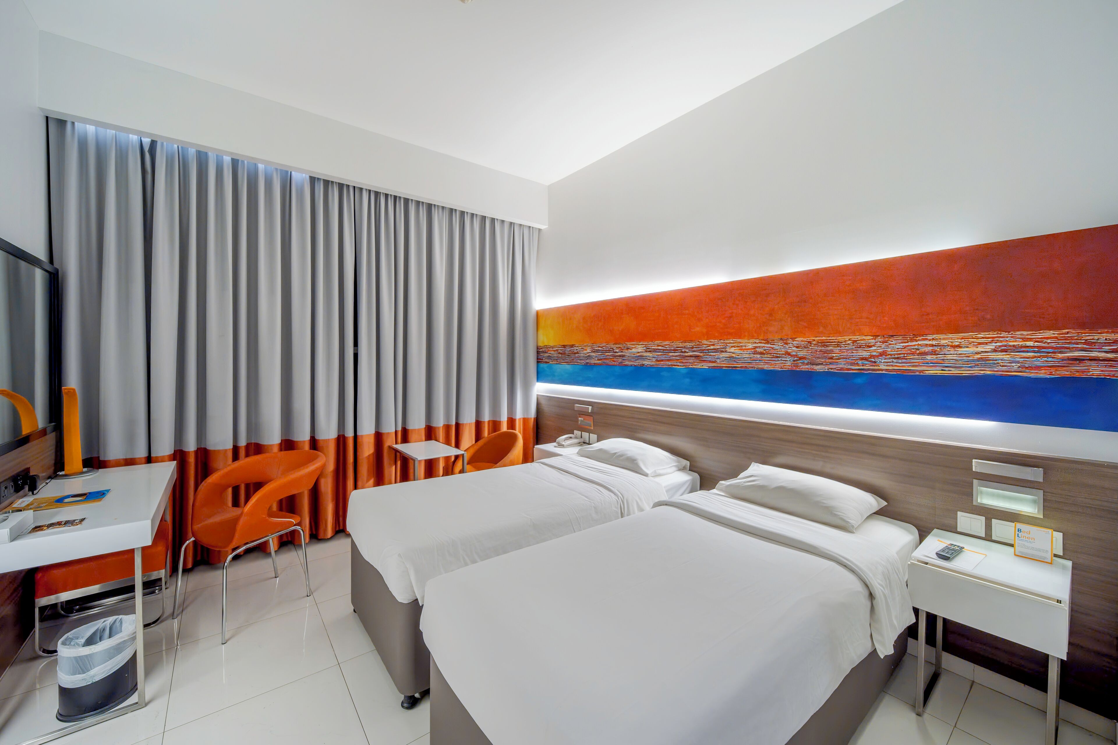 Ein Hotelzimmer mit zwei Betten, einem Schreibtisch, einem Sessel und einem großen Gemälde an der Wand.